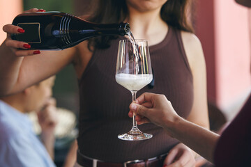 close up shot of female sommelier pouring sparkling wine to guest on outdoor. Restaurant service concept.