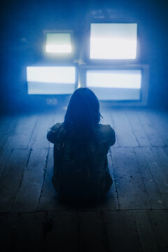 female person sitting alone on the floor in front of many displays or tv's in scary location