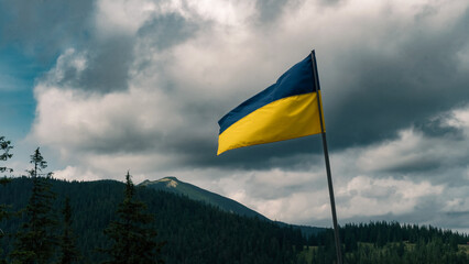 The Ukrainian flag waves proudly against the backdrop of forested mountains and dramatic skies. This scene evokes a strong sense of national pride and resilience.