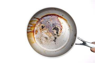 Dirty, oil and grease burnt bits and stains on a metal frying pan. Held in hand by male hand. Close up studio shot, isolated on white