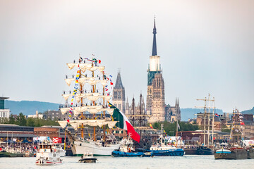 Obraz premium ROUEN, NORMANDY, FRANCE - JUNE 8, 2023: festive arrival of Mexican navy training ship Cuauhtemoc, in downtown river harbour, sailors manning the yards, tall ship maneuvering in front of cathedral