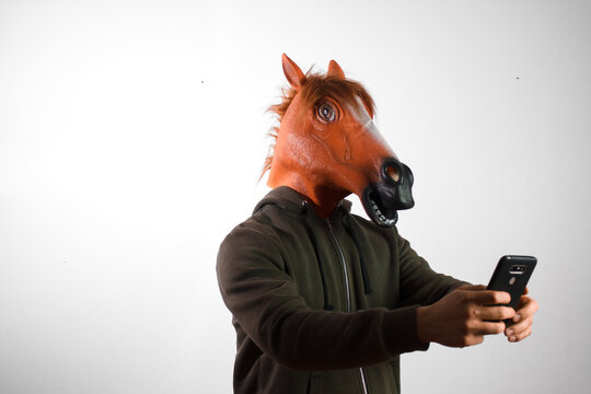 A man with a horse mask looking at a smartphone on a white background