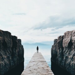 A lone figure stands on a stone pier surrounded by serene water and rocky cliffs.