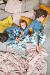 Two children tickle their little brother who laughs while looking at the camera.