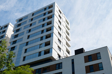 Modern high-rise apartment building against a blue sky with some trees visible in the foreground