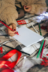 Woman in a knitted sweater sitting on a cozy plaid blanket with Christmas toys and gift box,...