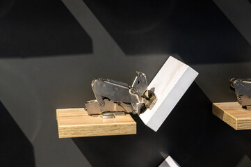 Metal hinge mechanism on wooden block displayed against dark background.