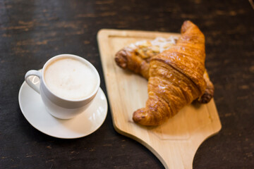 Croissant and cup of hot cappuccino On black wooden desk at breakfast.