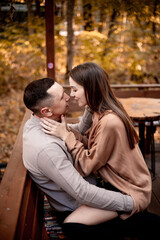 a young couple guy with a girl in autumn in a cafe in brown and orange tones on an outdoor terrace hugging and kissing, love or Valentine's day