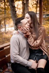 Fototapeta premium a young couple guy with a girl in autumn in a cafe in brown and orange tones on an outdoor terrace hugging and kissing, love or Valentine's day