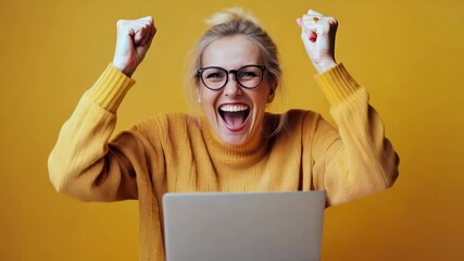 Middle aged woman waves her hands in joy in joy and rejoices over winning while sitting in front of laptop wearing yellow sweater isolated on yellow empty background with space for text
