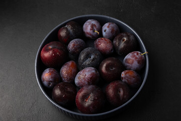 Juicy ripe fresh plum with water drops in gray plate on black background. Seasonal fruits. Selective focus, close-up.