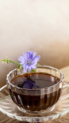 Close up figured glass cup with chicory tea and flower on beige vertical background with copy space.