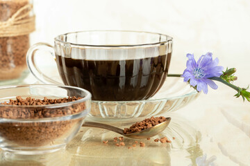 Close up soluble granulated chicory tea in glass cup on glass table. Herbal medicine for wellbeing.