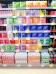 Blurred view of a supermarket aisle displaying a variety of colorful packaged goods on neatly arranged shelves.