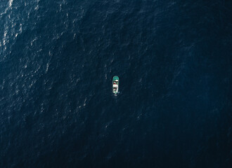 Aerial view of small fishing boat standing in the ocean - horizontal photo. Photo of green boat in the deep ocean water.
