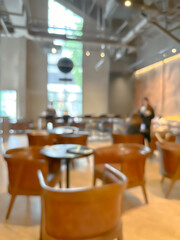 Blurred interior of a modern cafe with wooden chairs and tables, warm lighting, and large windows, creating a cozy and inviting atmosphere for social gatherings and relaxation.