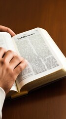 Hands gently clasped over an open Bible on a table, accompanied by a cup, conveying a moment of reflection and tranquility in soft, natural light