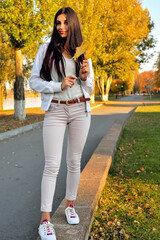 young beautiful girl walking on concrete parapet in autumn park in rays of sunlight