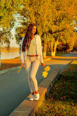 young beautiful girl walking on concrete parapet in autumn park in rays of sunlight