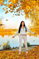 young beautiful girl in the park on the river bank throws yellow maple leaves