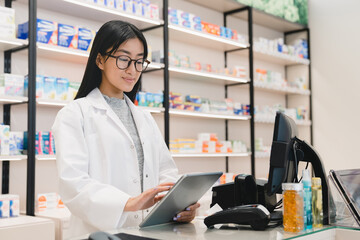 Female asian young druggist pharmacist using digital tablet for checking looking for active...