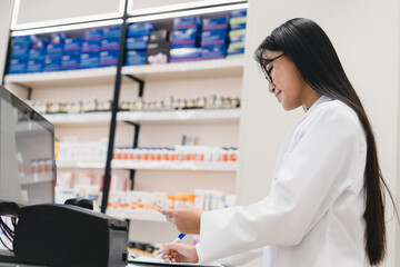 Side view of asian female young pharmacist druggist checking drugs medicines pills remedies on...