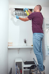 Man cleaning and maintaining air condition unit at home.
