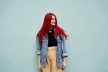 Young woman with vibrant red hair standing against a pastel blue wall