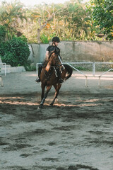 Teenage girl is riding a brown horse in an outdoor arena, practicing her horseback riding skills....