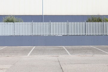 Fence made of gray plaster wall and metal railing with large slats on top. White and gray building...