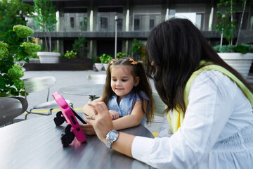 Mother and daughter enjoy a tablet together outside a modern building during the day