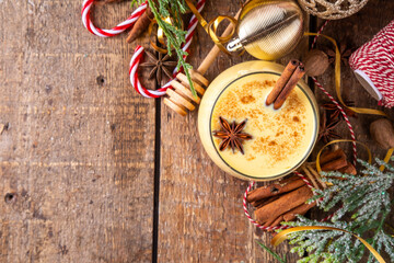 Christmas drink with cinnamon sticks and anise stars, two glasses of sweet classic eggnog cocktail on Christmas, New Year decorated background with fir tree and baubles