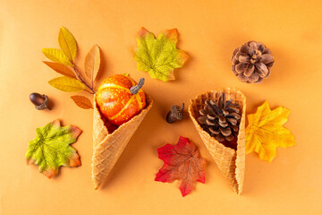 Autumn holidays concept. Autumn background with ice cream cones, pine cones, pumpkins, acorns and autumn leaves, on beige background, top view flat lay copy space