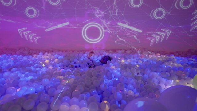 happy little girl playing in ball pool with projection mapping wall inside modern indoor playground.
