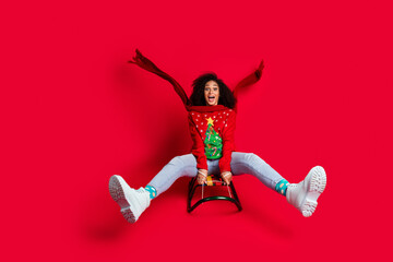 Photo of crazy funky cheerful girl wear ugly ornament sweater riding sleigh christmas festive event isolated on red color background