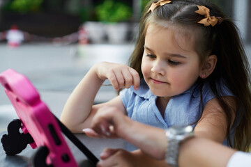 Young girl concentrates on a tablet, exploring its features at an outdoor play area