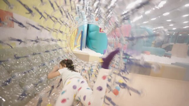 happy cheerful little girl playing zorbing bubble cylinder inside indoor playground.