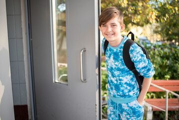 A 12 year old boy enters the entrance. A child with a backpack opens the door of the entrance. In autumn.