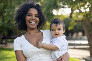 Beautiful portrait of smiling mother looking at camera while holding baby in a park