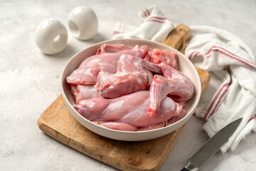 A raw rabbit cut into portions in a white ceramic bowl on a bright kitchen table in closeup