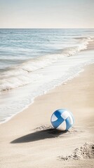 Obraz premium A blue and white beach ball sits on a sandy beach, with a view of the ocean behind it.