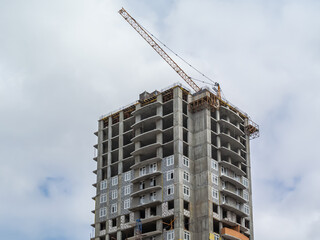 A tower construction crane next to a high-rise building under construction. The frame of the building under construction next to the crane. The structure of the building is made of reinforced concrete