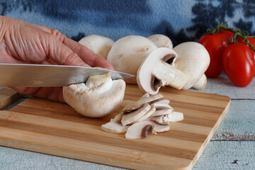 A close-up view of a hand slicing fresh white mushrooms on a wooden cutting board. 