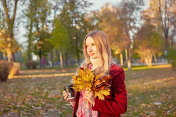 A woman in a red coat and a black skirt walks in an autumn park. The concept of autumn and the beauty of nature.