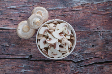 A top view of a bowl filled with freshly sliced mushrooms, placed on a rustic wooden table. 