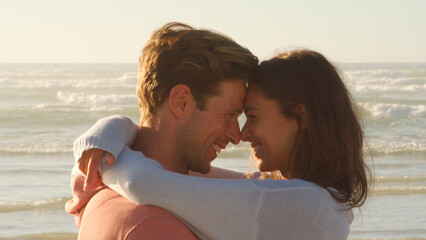 Casually Dressed Friends Or Couple Sitting On Winter Beach With Crashing Waves Behind
