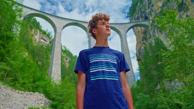 A teenage boy stands in front of the world famous Landwasser Viaduct in Switzerland in the summer