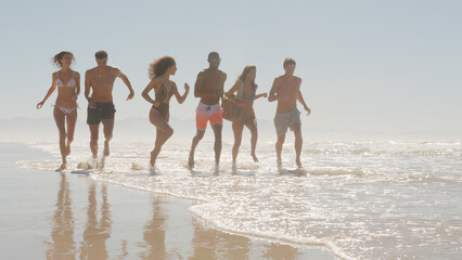 Group Of Friends In Swimwear Run Through Waves Together On Summer Beach Vacation