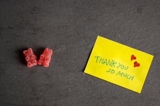 Vista superior de la nota adhesiva amarilla escrita gracias en un fondo de piedra con dos osos de gominola rojos